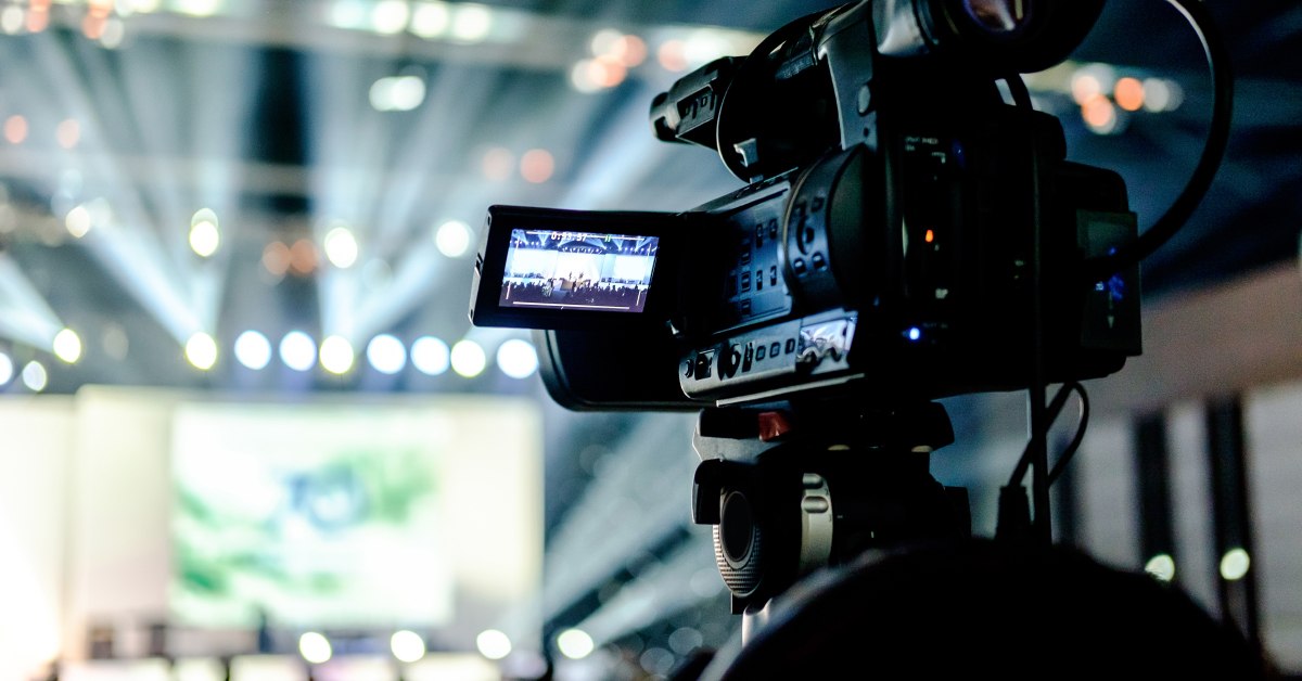 Video camera on tripod facing stage.